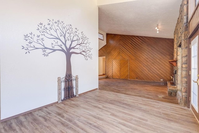 spare room with hardwood / wood-style floors, high vaulted ceiling, a textured ceiling, and wooden walls