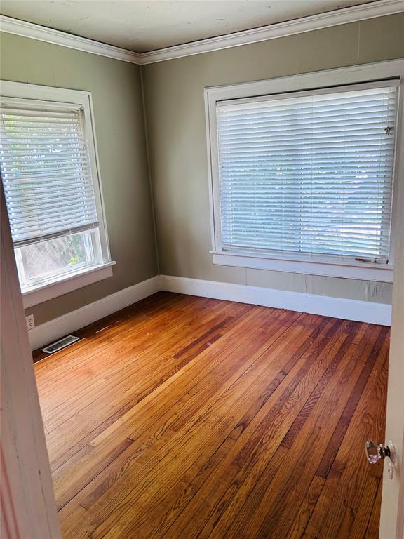 empty room featuring ornamental molding, light wood-type flooring, visible vents, and baseboards