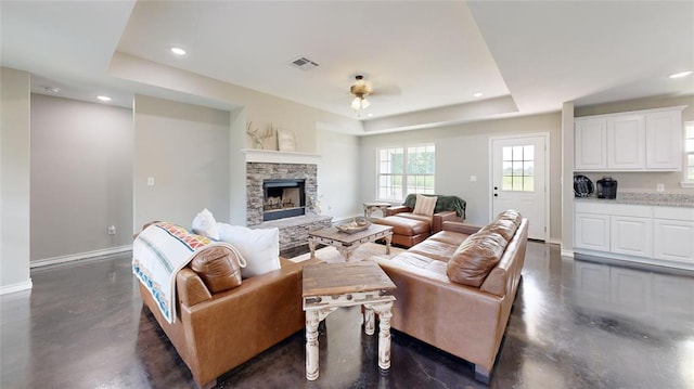 living room with a fireplace, a raised ceiling, and ceiling fan