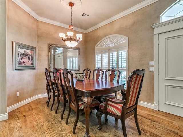 dining room with light hardwood / wood-style floors, a wealth of natural light, ornamental molding, and a notable chandelier