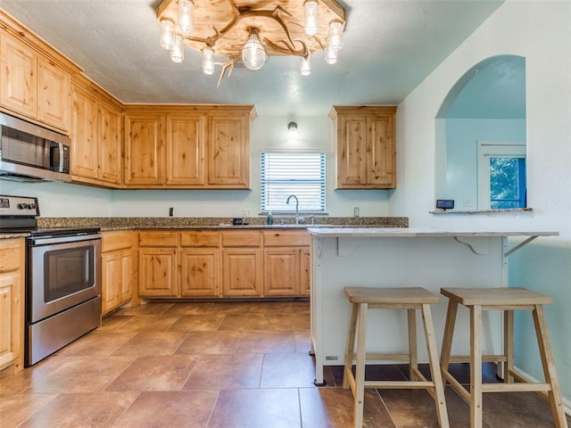 kitchen with a breakfast bar, light brown cabinets, stainless steel appliances, and sink