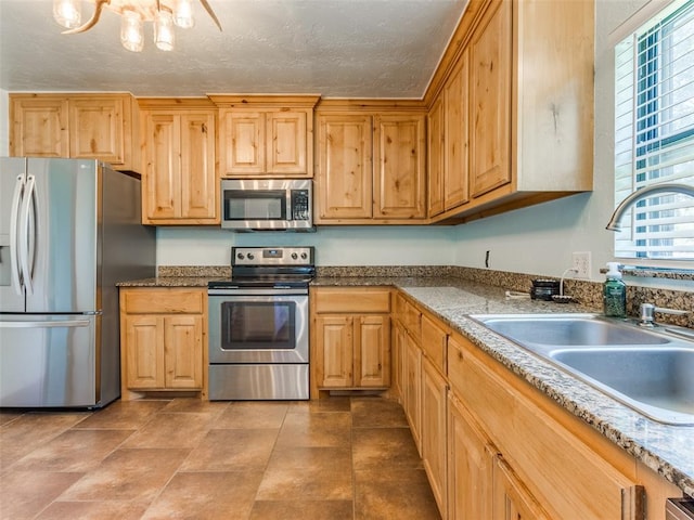 kitchen featuring light stone countertops, appliances with stainless steel finishes, a textured ceiling, sink, and a notable chandelier