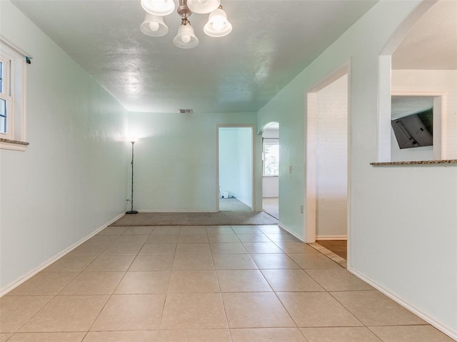 tiled spare room featuring an inviting chandelier