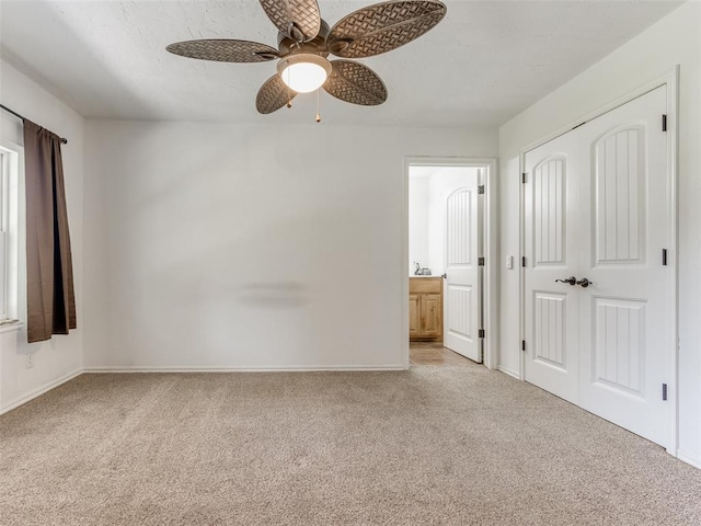 unfurnished bedroom featuring ceiling fan, light colored carpet, ensuite bathroom, and a closet