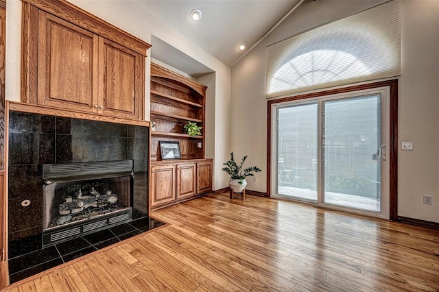 living room with light hardwood / wood-style floors, lofted ceiling, and a tiled fireplace