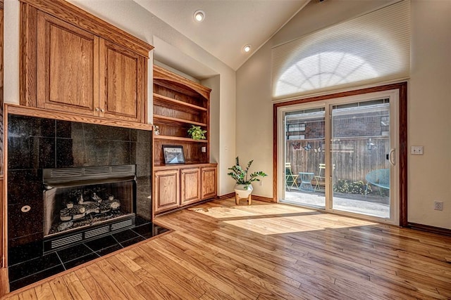 living room featuring built in shelves, light wood-type flooring, lofted ceiling, and a tiled fireplace