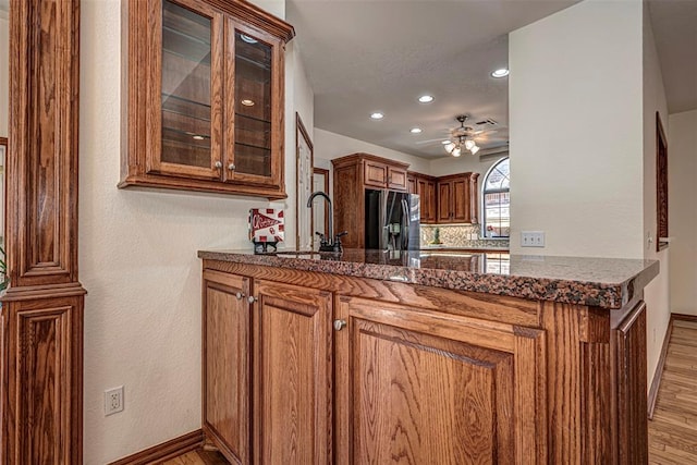 kitchen featuring black refrigerator with ice dispenser, ceiling fan, sink, dark stone countertops, and light hardwood / wood-style floors