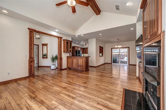 unfurnished living room featuring beamed ceiling, ceiling fan with notable chandelier, a tiled fireplace, and light hardwood / wood-style flooring