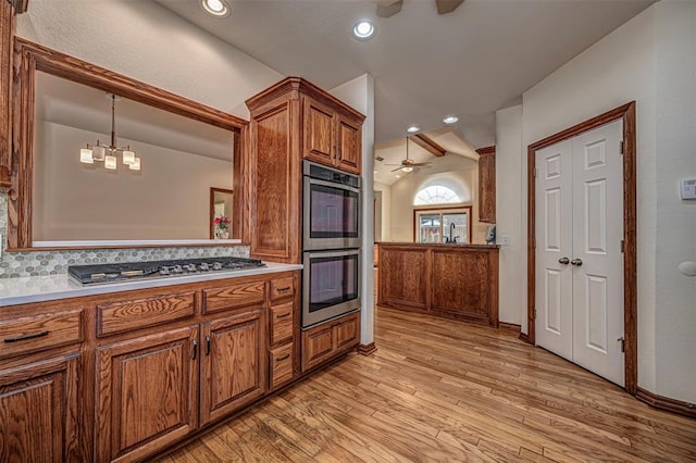 kitchen with hanging light fixtures, light wood-type flooring, decorative backsplash, ceiling fan with notable chandelier, and appliances with stainless steel finishes