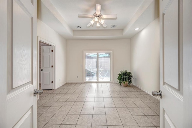 empty room with a tray ceiling, ceiling fan, and light tile patterned flooring