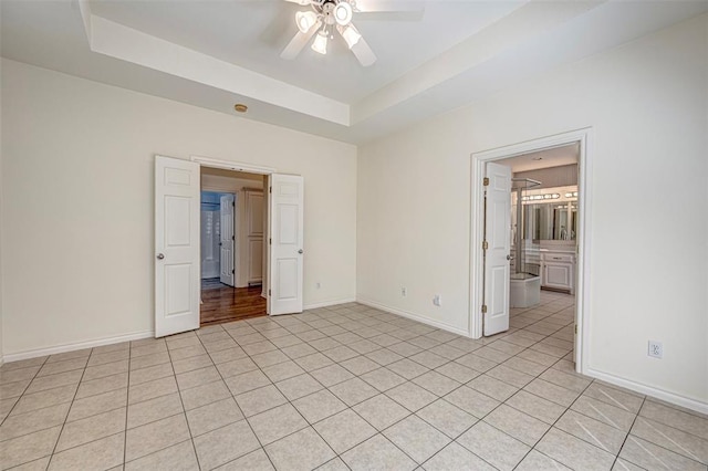 empty room with a raised ceiling, ceiling fan, and light tile patterned flooring