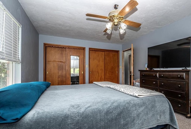 carpeted bedroom with a textured ceiling, two closets, and ceiling fan