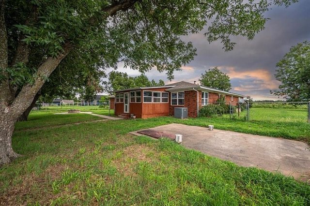 view of front of home featuring a sunroom, a yard, and central AC