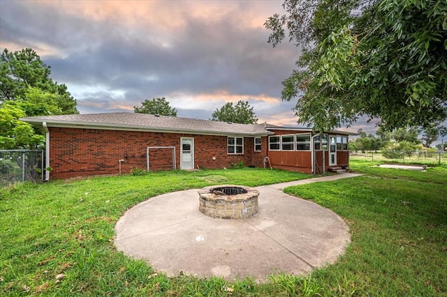 back house at dusk with a sunroom, a yard, a patio, and an outdoor fire pit