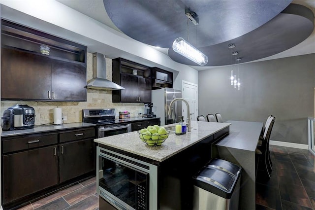 kitchen featuring appliances with stainless steel finishes, a center island with sink, tasteful backsplash, and wall chimney exhaust hood