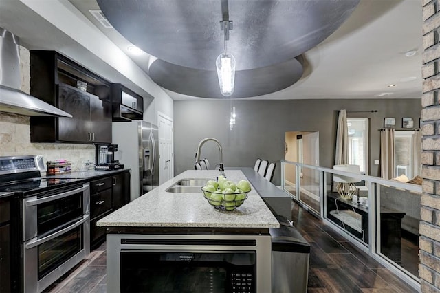 kitchen featuring wall chimney exhaust hood, sink, an island with sink, and stainless steel appliances