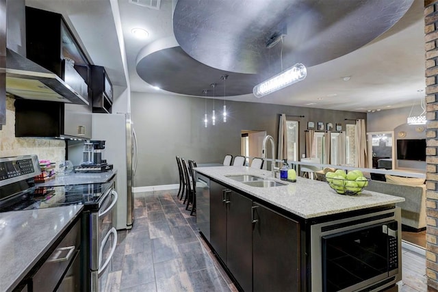 kitchen with sink, wall chimney exhaust hood, pendant lighting, a center island with sink, and appliances with stainless steel finishes