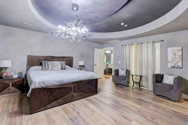 bedroom featuring a chandelier, a raised ceiling, ensuite bath, and light hardwood / wood-style flooring