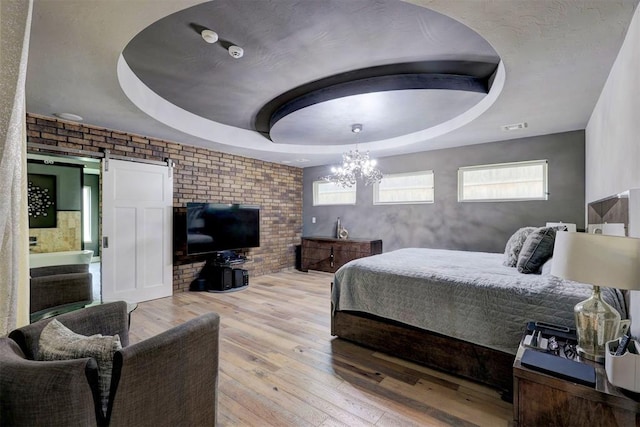 bedroom with a barn door, light hardwood / wood-style floors, multiple windows, and a tray ceiling