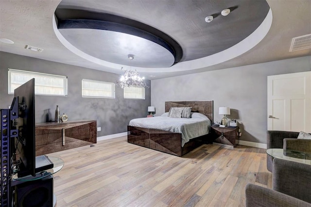 bedroom with a notable chandelier, light wood-type flooring, and a tray ceiling