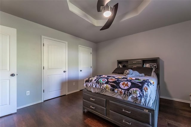 bedroom with a raised ceiling, dark hardwood / wood-style floors, and ceiling fan