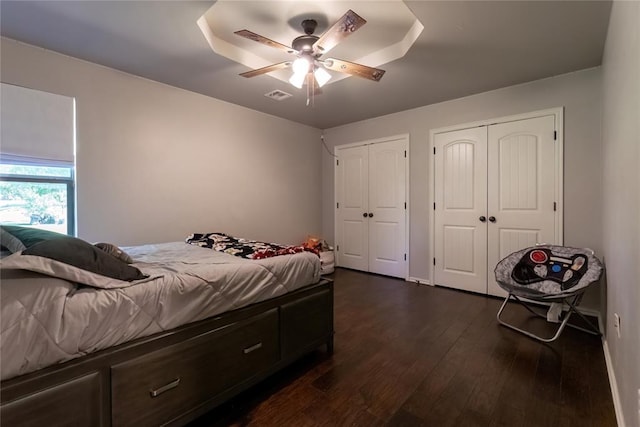 bedroom with two closets, dark wood-type flooring, and ceiling fan