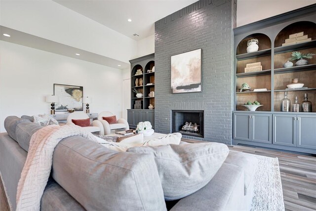 living room with a brick fireplace, light hardwood / wood-style floors, and built in features