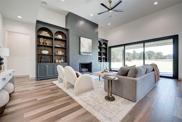 living room with built in shelves, ceiling fan, light hardwood / wood-style floors, and a fireplace