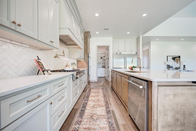 kitchen with a center island with sink, decorative backsplash, light hardwood / wood-style floors, white cabinetry, and stainless steel appliances