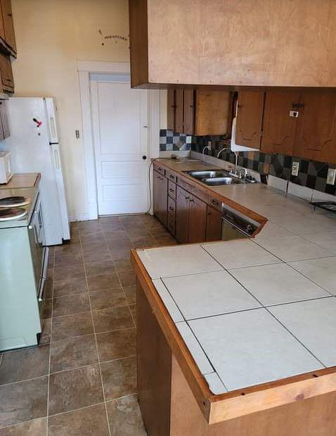 kitchen with kitchen peninsula, backsplash, white appliances, sink, and tile countertops