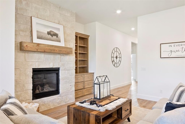 living room featuring built in shelves, a large fireplace, and light hardwood / wood-style floors