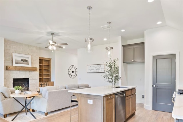 kitchen featuring sink, light hardwood / wood-style flooring, dishwasher, a stone fireplace, and an island with sink