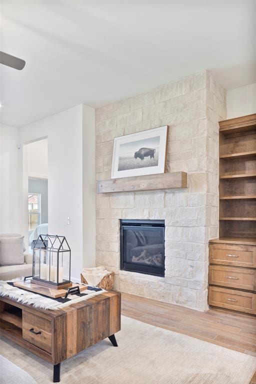 living room with light hardwood / wood-style flooring, a stone fireplace, and ceiling fan