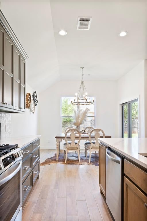 kitchen with vaulted ceiling, light hardwood / wood-style flooring, decorative light fixtures, stainless steel appliances, and a chandelier