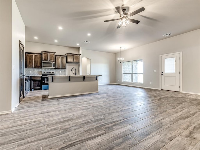 kitchen featuring ceiling fan with notable chandelier, light wood-type flooring, stainless steel appliances, and an island with sink