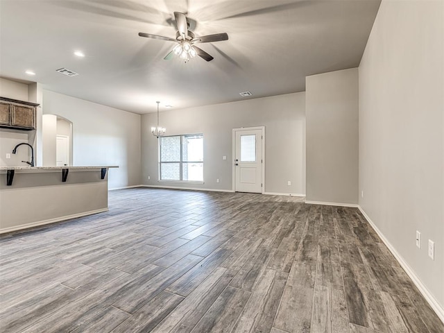 unfurnished living room with sink, ceiling fan with notable chandelier, and light wood-type flooring