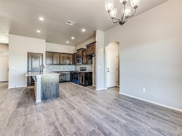 kitchen featuring an inviting chandelier, light hardwood / wood-style flooring, an island with sink, dark brown cabinets, and appliances with stainless steel finishes