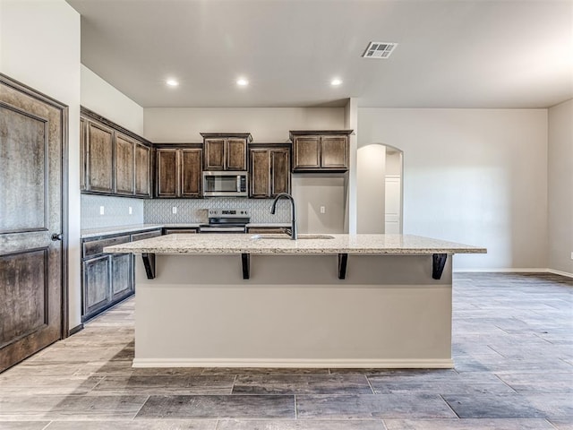 kitchen with a center island with sink, sink, light stone countertops, and stainless steel appliances