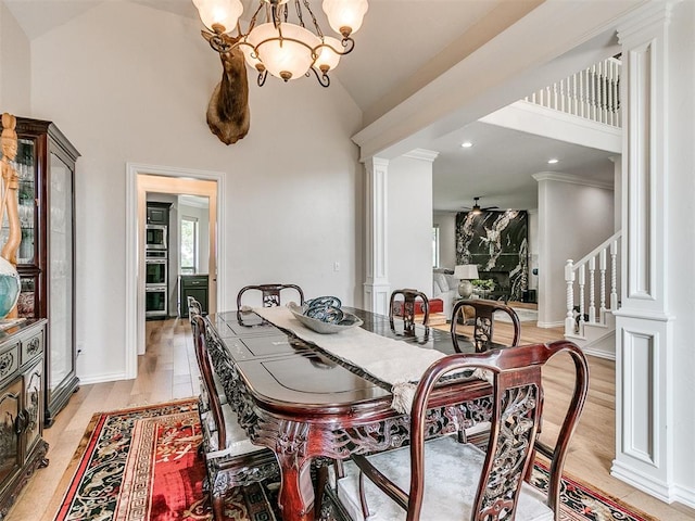 dining area with light hardwood / wood-style floors, decorative columns, high vaulted ceiling, and an inviting chandelier