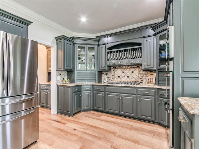 kitchen with light stone countertops, appliances with stainless steel finishes, light wood-type flooring, backsplash, and gray cabinets