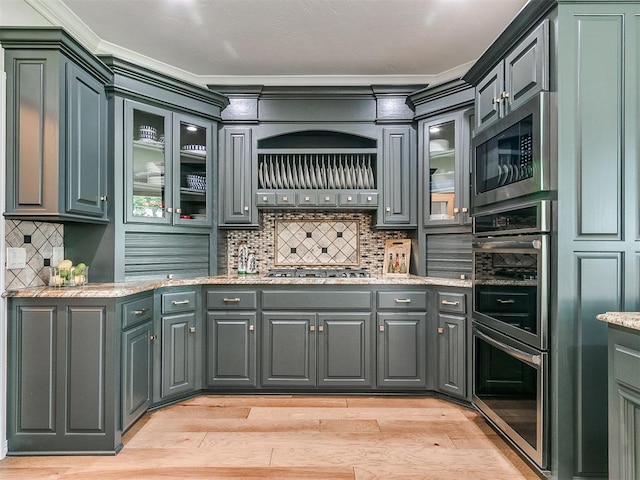 kitchen with gray cabinetry, light stone countertops, tasteful backsplash, appliances with stainless steel finishes, and light wood-type flooring