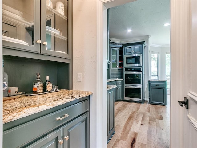 kitchen with appliances with stainless steel finishes, light wood-type flooring, light stone counters, and ornamental molding