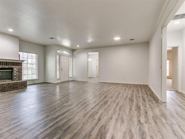 unfurnished living room featuring crown molding, light hardwood / wood-style flooring, a textured ceiling, and a brick fireplace