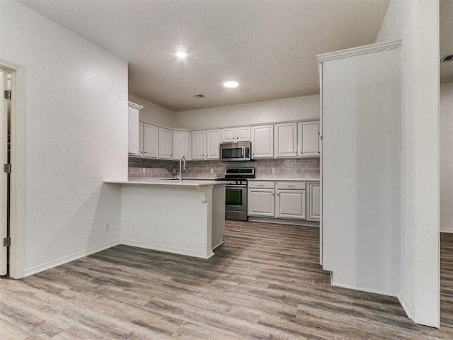 kitchen featuring hardwood / wood-style floors, backsplash, white cabinetry, kitchen peninsula, and stainless steel appliances