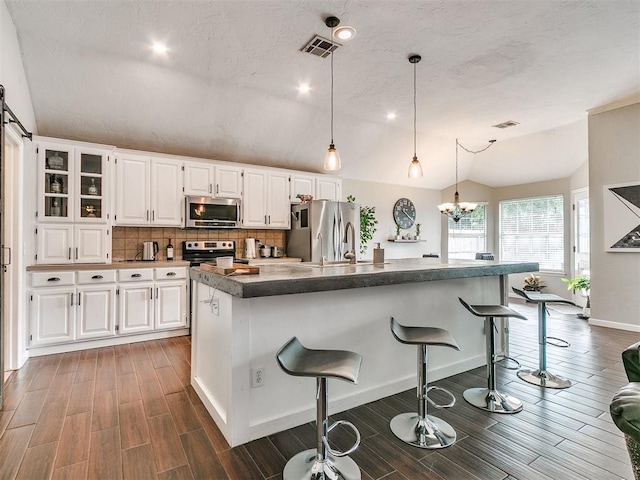 kitchen featuring a kitchen breakfast bar, white cabinets, vaulted ceiling, and appliances with stainless steel finishes