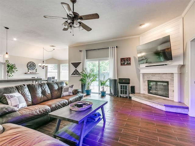 living room with dark wood-type flooring, a stone fireplace, crown molding, lofted ceiling, and ceiling fan with notable chandelier