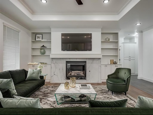 living room with a fireplace, built in features, hardwood / wood-style flooring, a tray ceiling, and crown molding