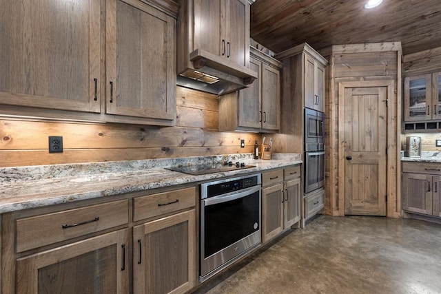 kitchen featuring black electric cooktop, light stone countertops, stainless steel microwave, and wooden walls