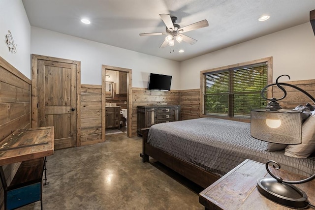 bedroom featuring ceiling fan, wood walls, and ensuite bathroom