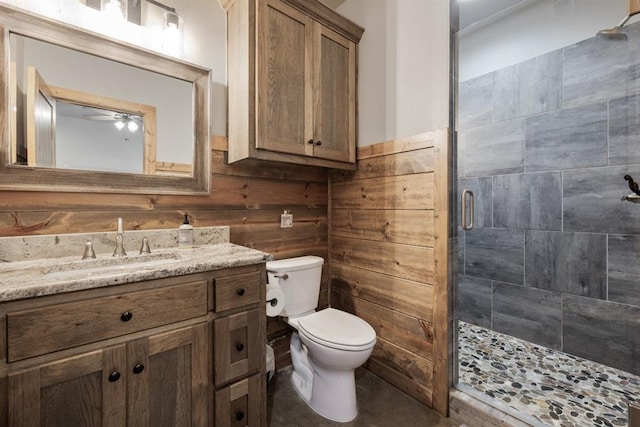 bathroom featuring vanity, wooden walls, ceiling fan, toilet, and an enclosed shower